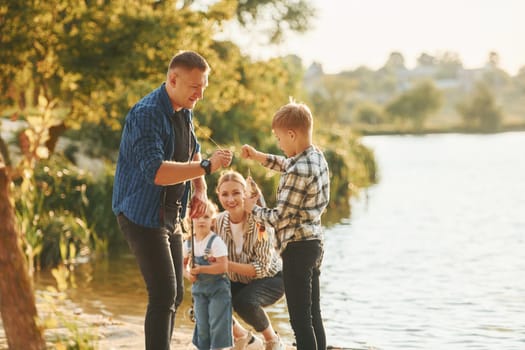 Rural scene. Father and mother with son and daughter on fishing together outdoors at summertime.