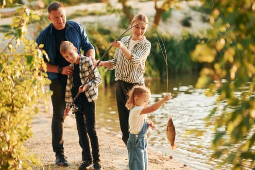 In casual clothes. Father and mother with son and daughter on fishing together outdoors at summertime.