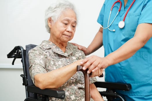 Doctor help Asian elderly disability woman patient holding walking stick in wrinkled hand at hospital.