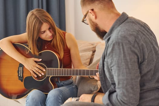 Guitar teacher showing how to play the instrument to young woman
