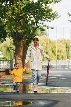 Mother with her son is having a walk outdoors in the park after the rain.