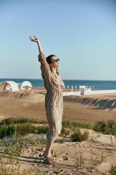 stylish woman in beige dress posing with arms raised high in windy weather in nature. High quality photo
