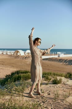 woman in a beige dress posing standing on the seashore in sunglasses in windy weather. High quality photo