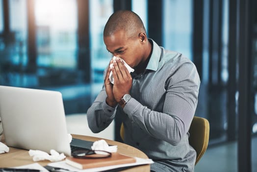 This runny nose is ruining my day. a young businessman blowing his nose while working in an office.