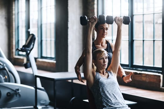 Lifting weights are great for the arms. a mature woman lifting weights with a female instructor at the gym.