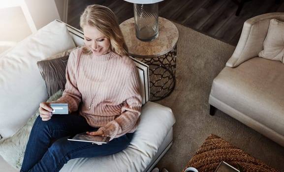 Shopping and comfort, the bet of both worlds. a mature woman using a credit card and digital tablet while relaxing at home.