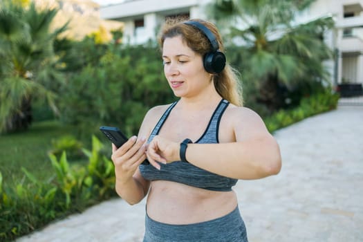 Young plus size woman with smart watch. Girl training in park. Woman check in fitness tracker