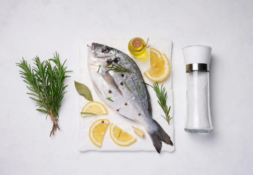 Raw whole dorado fish on white board and spices for cooking, top view on white table