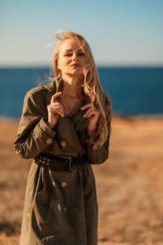 Portrait blonde sea cape. Calm young blonde in a khaki raincoat stands on the seashore