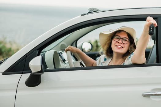Car driver woman smiling showing new car keys and car. Female driving rented cabrio on summer vacation