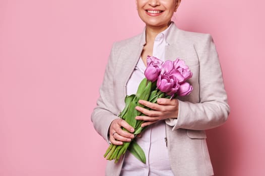 Details on bouquet of tulips for festive occasion in the hands of beautiful smiling woman, isolated over pink background