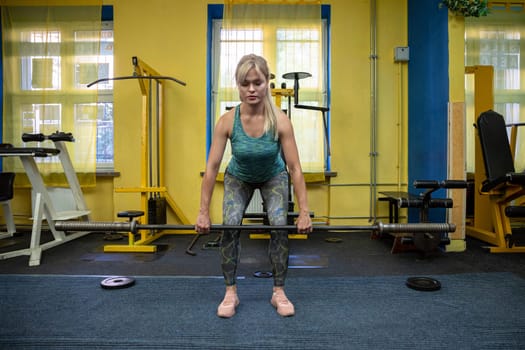 Athletic blonde in gym lifts barbell without load