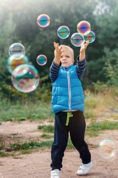 The little boy catches soap bubbles in autumn nature.