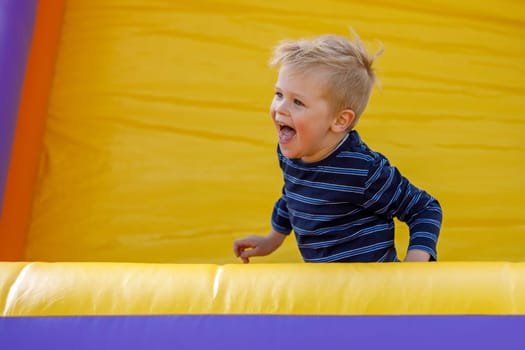 Stormy child be naughty on playground trampoline. Little cool boy have fun on a yellow inflatable trampoline.