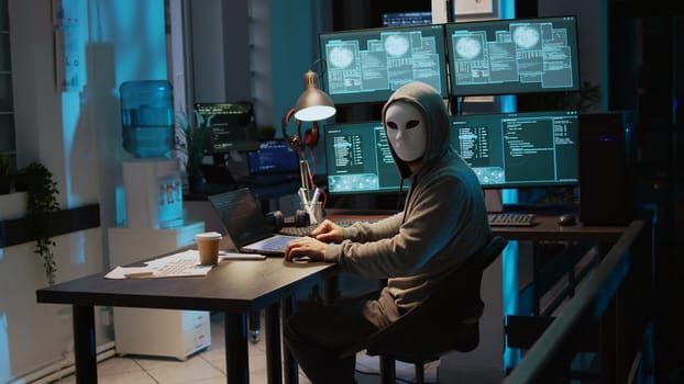 Male criminal wearing mask and hood to hack computer system
