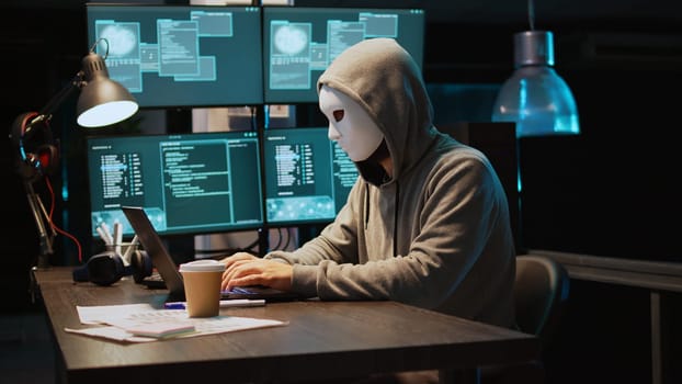 Cyber scammer wearing mask and hood to hack computer system