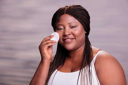 Smiling body positive woman removing cosmetics with cotton pad
