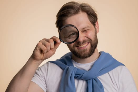 Investigator researcher man with magnifying glass near face, looking into camera with big zoom eye