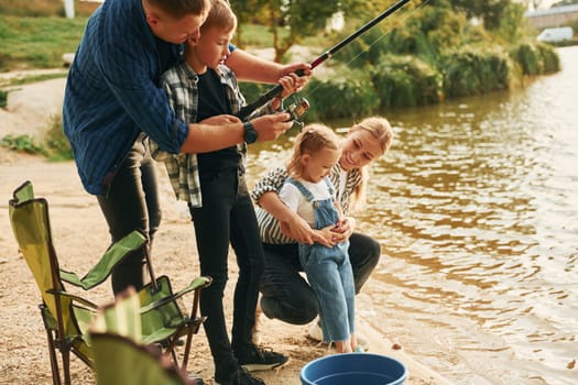 Learning to fishing. Father and mother with son and daughter together outdoors at summertime.