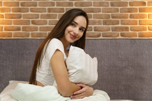Young woman hugging a pillow on a comfortable bed with white linens