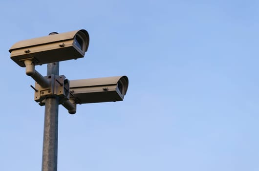 Surveillance cameras mounted on a pole against the blue sky.