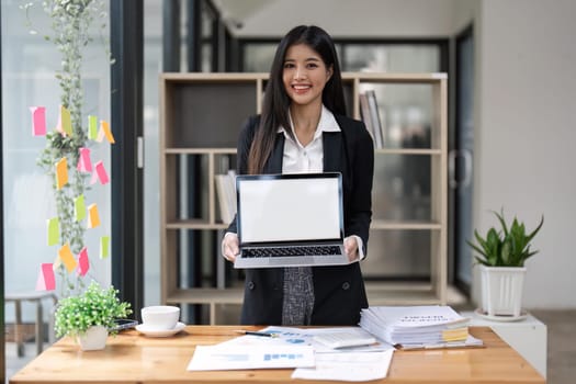 attractive Asian young business woman at her office desk workspace with a notebook laptop computer. Notebook blank screen mockup