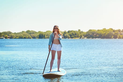 This is my kinda adventure. an attractive young woman paddle boarding on a lake.