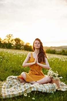 a woman in a chamomile field meditates holding her hands on her chest against the background of a sunset