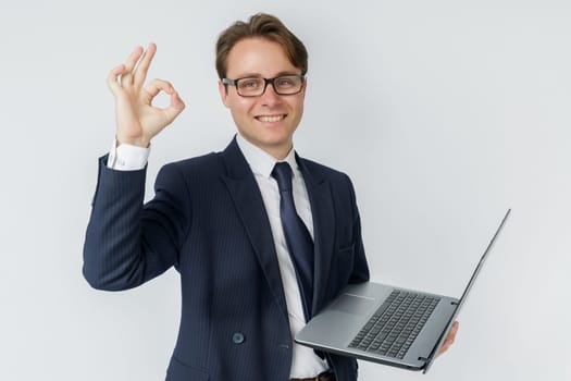 A businessman is holding a laptop, his other hand is showing OK gesture. White background.