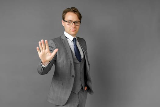 Portrait of a businessman in a suit who stretches out his hand in front of his palm. Stop. Gray background.