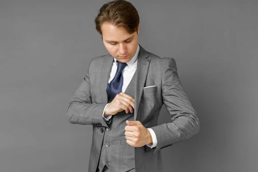 Portrait of a businessman in a suit who takes money from his inner pocket. Gray background.