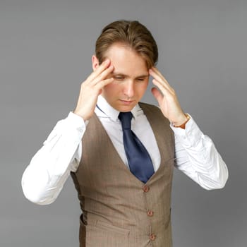 An emotional portrait of a businessman who touches his head with his hands. Gray background