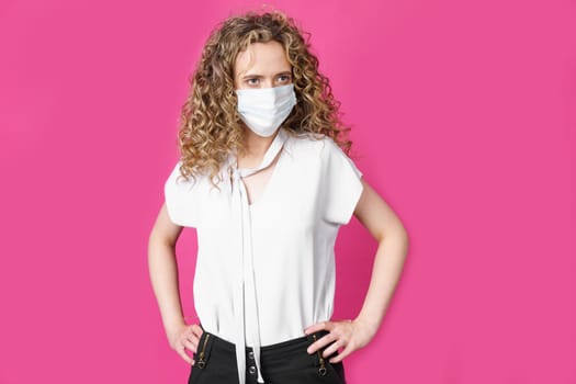 A young woman with a medical mask on her face is standing with her hands on her waist.