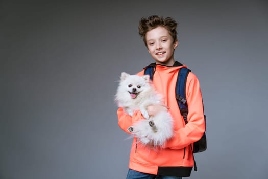 cheerful schoolboy with a backpack and a dog in his hands on a gray background