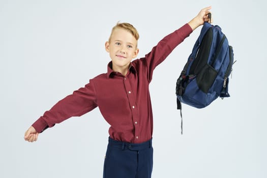 A schoolboy holds a schoolbag over his head.