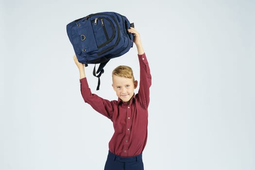 A schoolboy holds a schoolbag over his head.