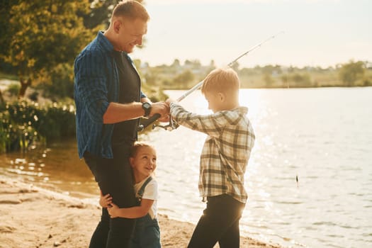 Father with son and daughter on fishing together outdoors at summertime.