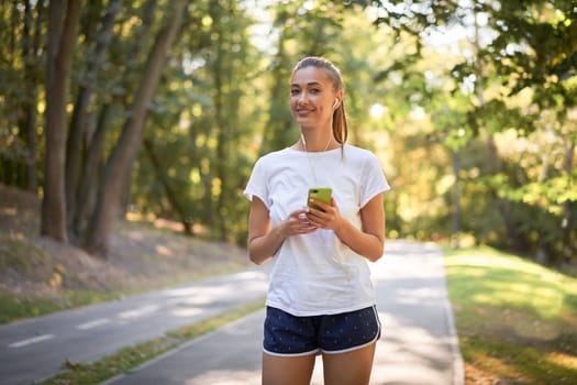 Woman putting on earphones to listen music before jogging summer park