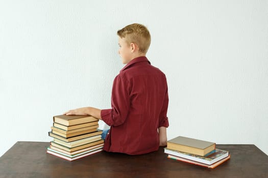 Pupil boy sits at the table with his back to the camera, next to the books.