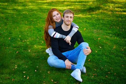 Happy young couple sit in an embrace in the park on the grass