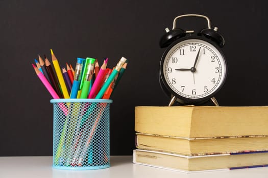 alarm clock stands on the books and glass with pencils on a black background