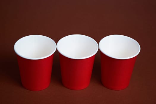Three red disposable cups on a dark brown background.