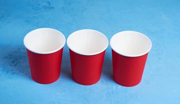 Three red disposable cups on a blue background. Place for text