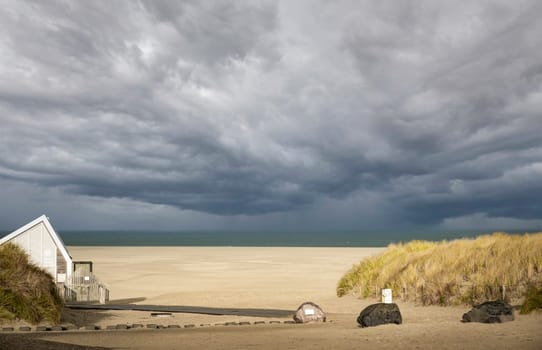 the access to the beach at the top on the island of Texel in the Netherlands with the dunes on the right and a beach house on the left with the horizon and the dark clouds in the background