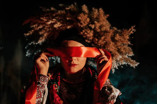Ukrainian woman ties red ribbon around eyes as on ritual doll motanka.