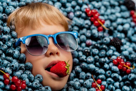 Little boy face in berries blueberries with strawberry, organic bilberry plant