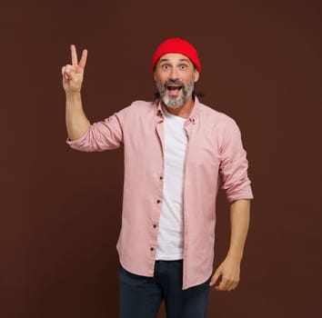 Positive European caucasian man handsome shows gesture of V victory. Cheerful man with silver beard raises his hand with two fingers V shape, indicating gesture of victory, with smile on face.