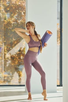 Standing and holding mat. Woman in sportive clothes doing yoga indoors.
