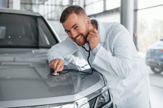Medic in white coat is using stethoscope on the automobile