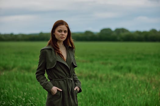 a beautiful woman stands in a green field and adjusts her coat